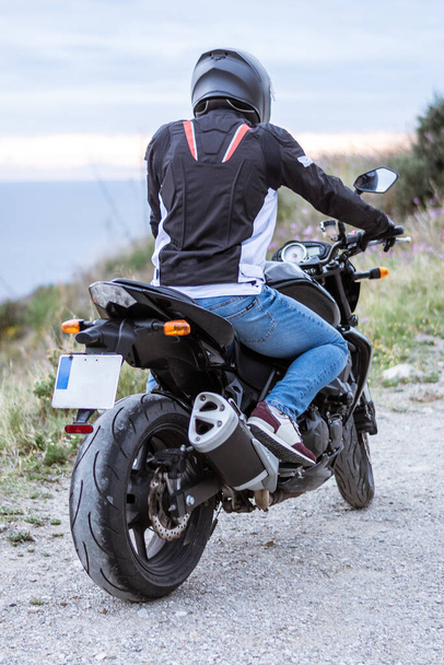 Joven motorista con su moto negra lista para conducir, frente al mar
 - Foto, Imagen