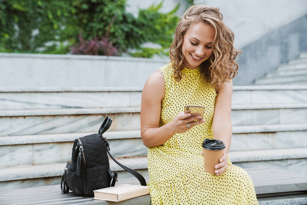 Woman sit outdoors drinking coffee using mobile phone. - Photo, Image