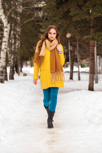 Young beautiful woman in yellow coat walking winter park - Photo, image