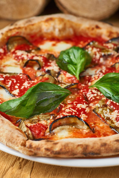 Traditional Italian pizza with eggplants, mozzarella, basil and tomatoes on wooden background - 写真・画像