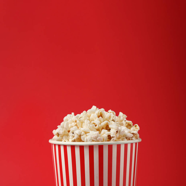 Delicious popcorn in paper cup on red background, closeup - Fotó, kép