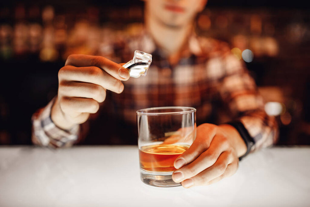 Barman mette pinze di ghiaccio con spruzzi nel bicchiere di whisky bar. Sfondo marrone scuro
 - Foto, immagini