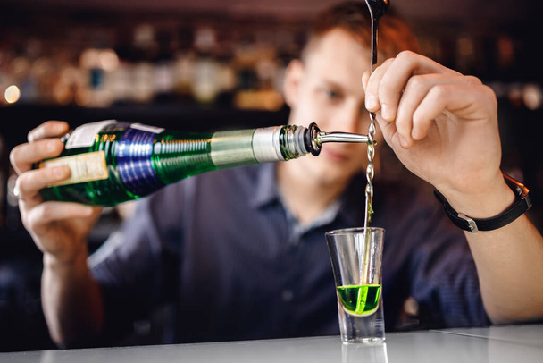 Bartender is preparing mix of cocktail with spoon of green alcohol in small glass, bar counter - Fotoğraf, Görsel