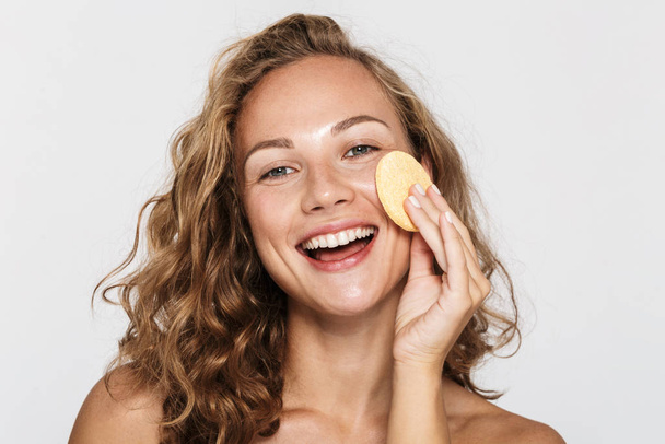 Image of positive half-naked woman smiling and using facial sponge - Photo, image