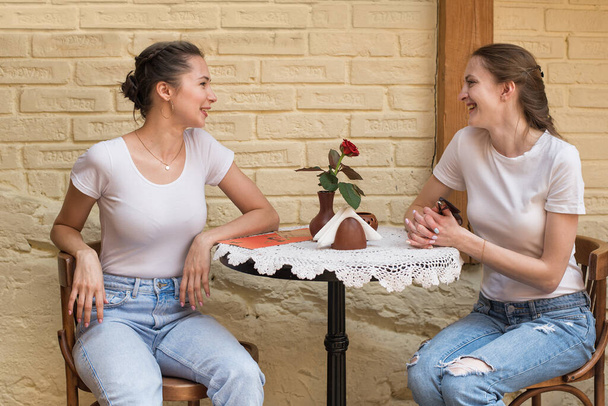 Две молодые женщины сидят за столом в кафе и разговаривают. Сплетни. Дружба
 - Фото, изображение