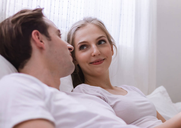 Happy young caucasian couple or lover on bed together. Man read book for woman in dreamy romantic moment in bedroom. Photo of married relationship or bonding between husband and wife in Valentine day - Photo, Image