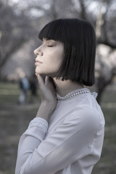 Short black hair model woman, posing in a blooming almond tree field - Foto, Imagen