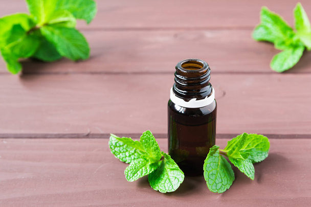 bottle with essential oil and mint leaves on a brown wooden table - Photo, Image