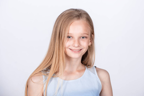 Cute European little girl waiting for mom to pick her up after dance classes. A beautiful female child with blonde hair in a blue t-shirt, standing casually over white background, being calm. - Фото, зображення