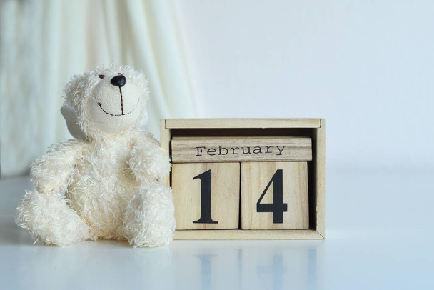 14 February text on wooden block calendar and bear.Valentine card.Template greeting card for Valentine's Day. Greeting card with white eustomas .copy space. Selective focus - 写真・画像