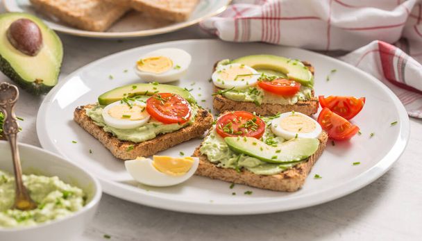 Healthy breakfast from toasts with avocado spread guacamole egg tomato and chives. - Foto, afbeelding
