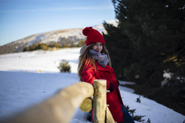 Kırmızı şapkalı bir kadın dağdaki ahşap bir çitte oturuyor. - Fotoğraf, Görsel