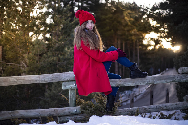 woman dressed in red with red cap sitting on a wooden fence in the mountain - Photo, Image