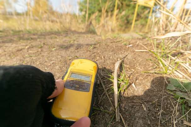 Compteur Yellowgeiger sur les mains montre des niveaux élevés de rayonnement près du sol en face de la forêt rouge en automne. Visite de groupe de la zone d'exclusion de Tchernobyl
. - Photo, image