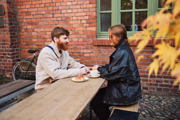 Young beautiful couple happily resting together drinking coffee in cozy street cafe - Photo, Image