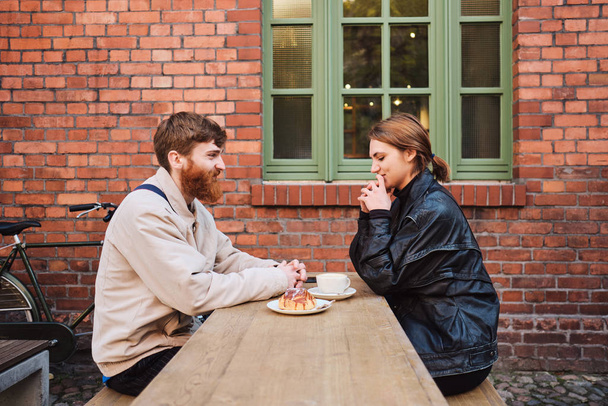 Vista lateral do jovem belo casal feliz descansando juntos no café de rua
 - Foto, Imagem