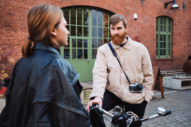 Bisikletli sakallı genç adam kız arkadaşıyla sokakta düşünceli bir şekilde konuşuyor. - Fotoğraf, Görsel