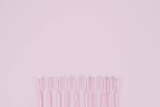 A row of disposable eyelash brushes on a pastel pink background with place for text. The concept of eyelash extension and makeup. Copyspace - Fotó, kép
