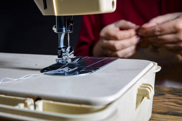 Las manos femeninas cosen un vestido azul en una máquina overlock profesional en un taller. Manos de costurera sosteniendo textil para coser ropa. Fondo borroso Vista de cerca del proceso de costura
. - Foto, Imagen