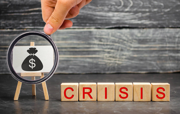 Wooden blocks with the word Crisis and the image of dollars. The concept of financial and economic crisis. capital outflow. sabotage of the economy. bankruptcy. cash loss. pay cut and lack of funds - Photo, image