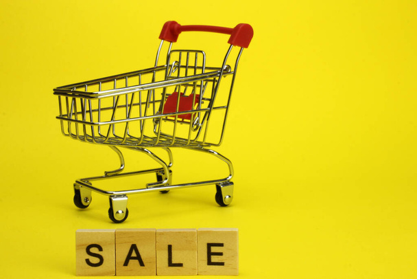 Mini supermarket cart, trolley on a yellow background. Purchases. The Word Sale - Photo, Image