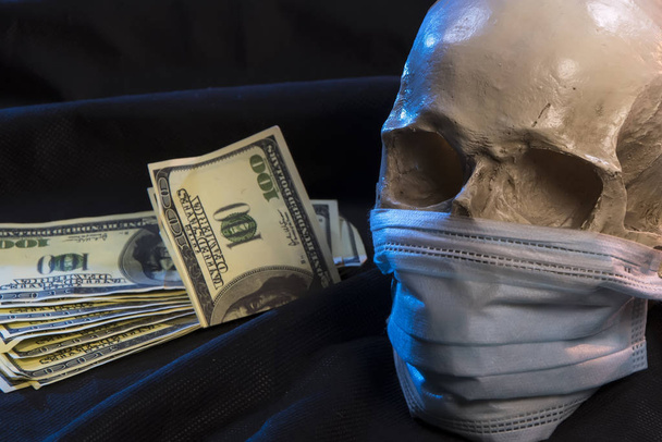 Un teschio umano con una maschera medica su sfondo scuro, vicino ai dollari americani. Concetto: la mortalità da coronavirus, la medicina pagata non salverà, le vittime di esperimenti medici, epidemie e atmosfera inquinata
. - Foto, immagini