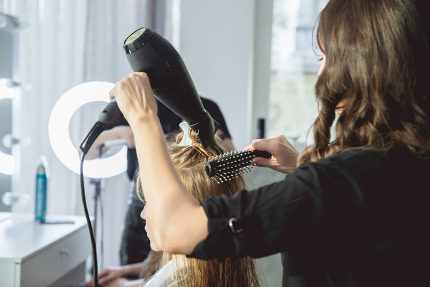 Крупним планом перукарські руки висушують довге світле волосся з сушаркою і круглою щіткою
 - Фото, зображення
