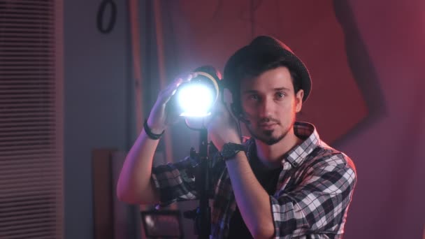 männlicher Filmemacher justiert professionelles Lichtgestell im Studio, mit eingeschalteter Beleuchtung - Filmmaterial, Video