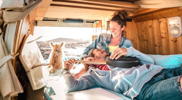 Hippie couple amd dog traveling together on vintage van transport at sunset - Life inspiration concept with guy and girl on minivan adventure trip with ukulele in relax moment - Warm sunshine filter - 写真・画像