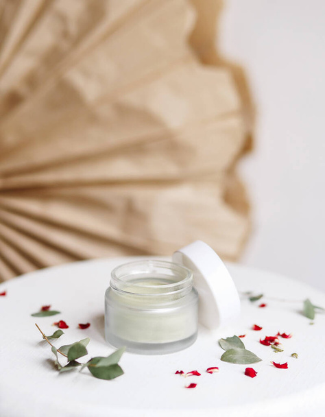 Poeder cosmetische masker. Glazen pot met matcha op een witte achtergrond met droge bloemblaadjes. - Foto, afbeelding