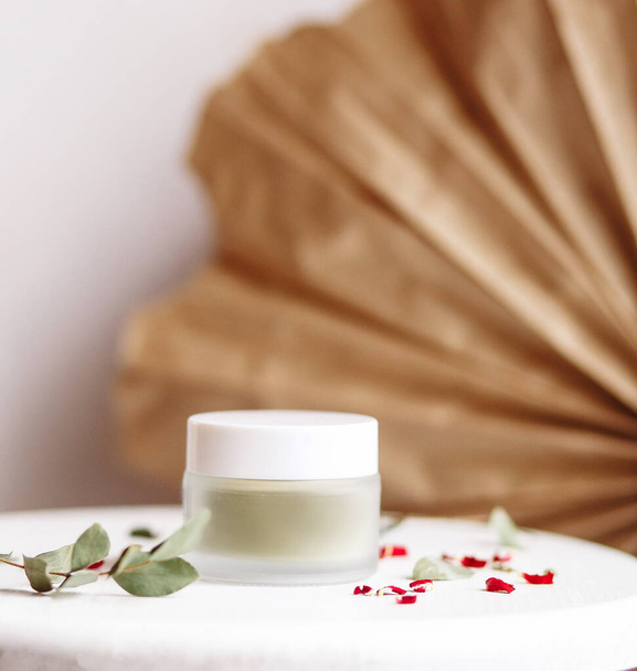 Powder cosmetic mask. Glass jar with matcha on a white background with dry petals. - Foto, afbeelding