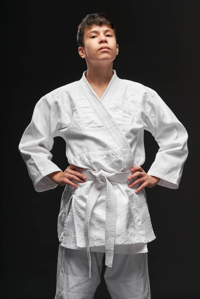 sport concept - a proud teenager dressed in martial arts clothing poses on a dark gray background, studio shoot - Photo, Image