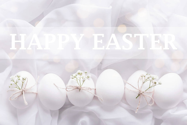 Bílá velikonoční vejce s květinami a zelené listy na bílém texturovaném pozadí - Fotografie, Obrázek
