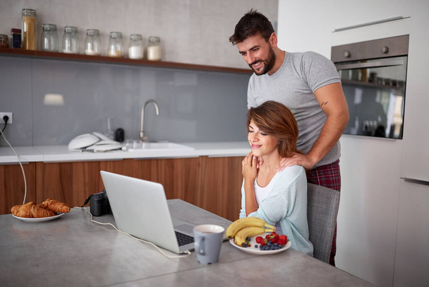 young adult couple watching content on laptop in kitchen. casual - Φωτογραφία, εικόνα