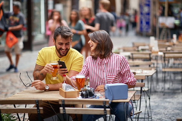 Man and  girl sitting at a cafe drinking beer and looking at pictures on a mobile phone. - Фото, изображение