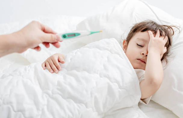 Grip hastası çocuk yatakta yatıyor ve annesi termometreyi tutuyor. - Fotoğraf, Görsel