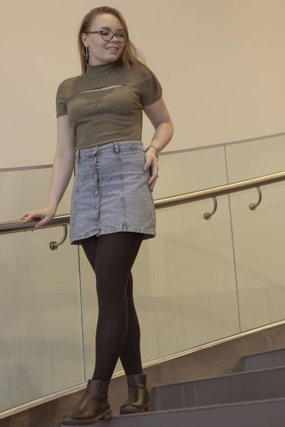 beautiful white girl with glasses stands on the stairs with transparent railing. - Photo, Image
