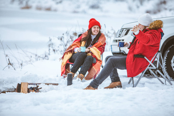 чоловік з жінкою, сидячи на стільцях біля багаття в зимовий час. автомобіль подорожі
. - Фото, зображення