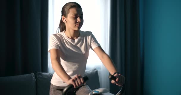 Active female looking at smart watch while riding static bike - Video, Çekim