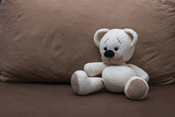 Um filhote de urso branco de malha em um sofá marrom macio
. - Foto, Imagem