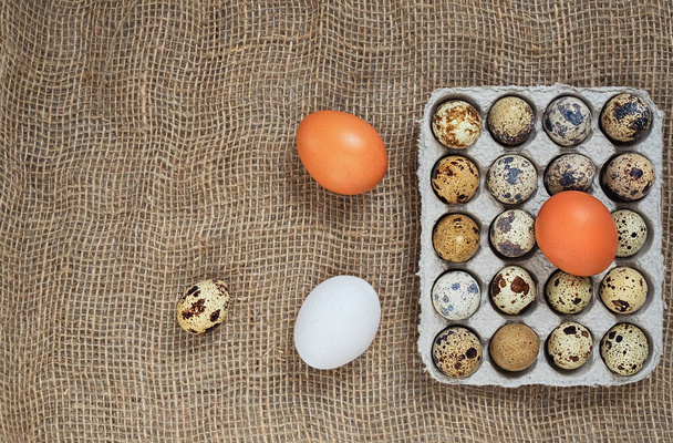 organická křepelčí vejce a hnědá a bílá kuřecí vejce nevařené čerstvosti výživa na lněném hnědém pytli pro texturu pozadí. soft focus, top view, copy space - Fotografie, Obrázek