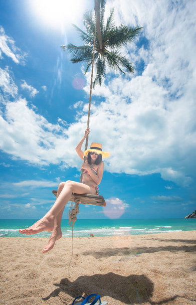 young woman playing around on wooden swing under palm tree at sunny on the island, summer time vacation and weekend relax funny happy time - Foto, immagini