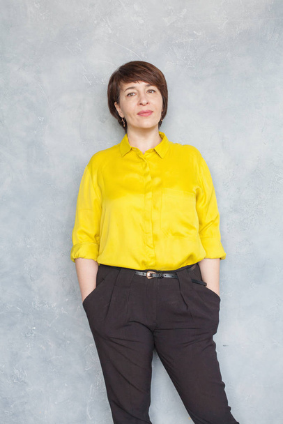 Уверенная деловая женщина в жёлтой рубашке, стоящая на сером
 - Фото, изображение