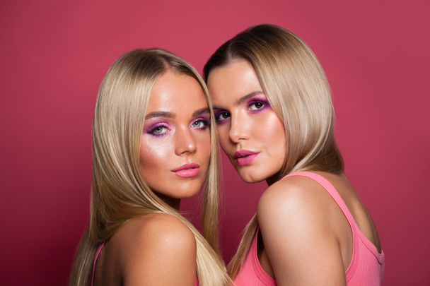 Twee blonde modellen met lang recht haar en make-up op roze  - Foto, afbeelding