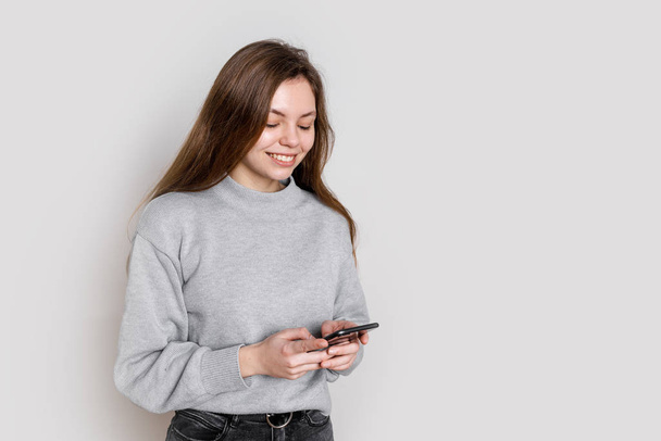 Cheerful young woman using smartphone in studio on white background. Millenial concept. Social media - Фото, зображення