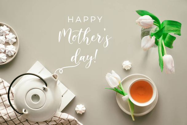 Mother;s day celebration, flat lay on table set for tea. Trendy modern flat lay, top view. Tea pot, sweets and white tulips on light grey. Sweet marshmallow decorations. - Φωτογραφία, εικόνα