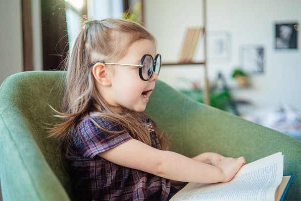 little toddler girl in glasses reading a book. back to school concept - Fotó, kép