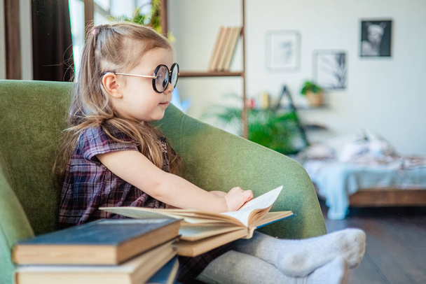 little toddler girl in glasses reading a book. back to school concept - 写真・画像