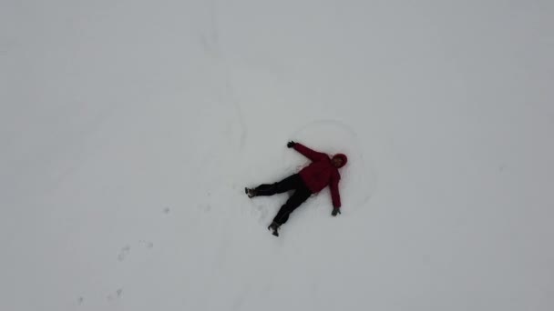 Veduta aerea di una donna sdraiata nella neve e le mani disegna le ali di un angelo. Divertimento invernale
 - Filmati, video