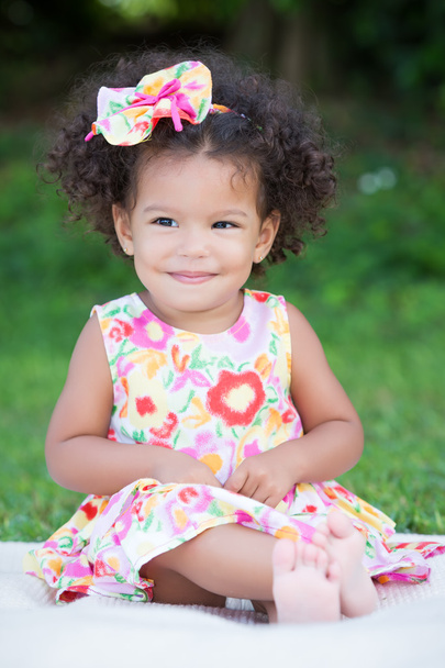 Niña pequeña con un peinado afro sentada en la hierba
 - Foto, imagen